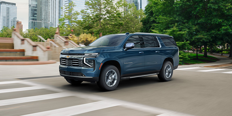Blue Chevrolet Suburban driving through a city street.