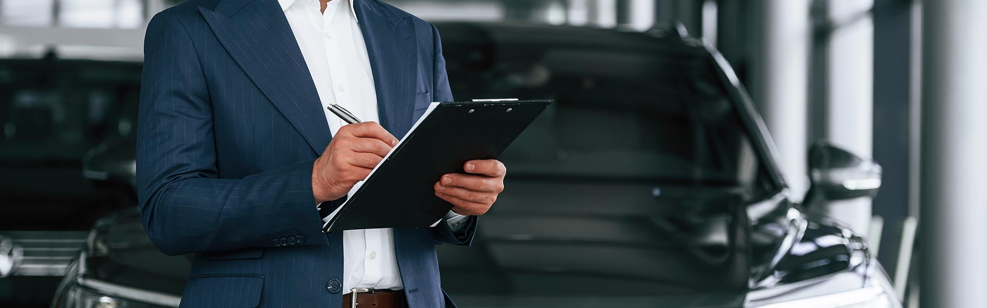 Salesperson writing on a clipboard at a car dealership